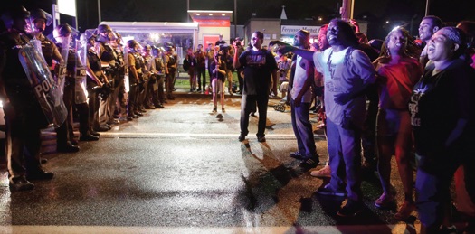 Demonstrators in Ferguson, Mo. yell as police form a line across West Florissant Ave., Aug. 9, before shots were fired near the protest marking the one-year anniversary of Michael Brown Jr.’s death. Photos: AP Wide World Photo/Jeff Roberson