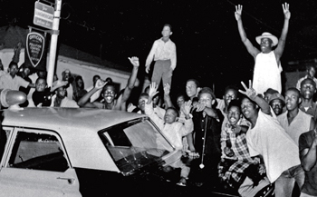 In this Aug. 12, 1965 file photo, demonstrators push against a police car after rioting erupted in the Watts district of Los Angeles. It began with a routine traffic stop 50 years ago this month. The Watts riot broke out Aug. 11, 1965. Photo: AP Wide World Photos